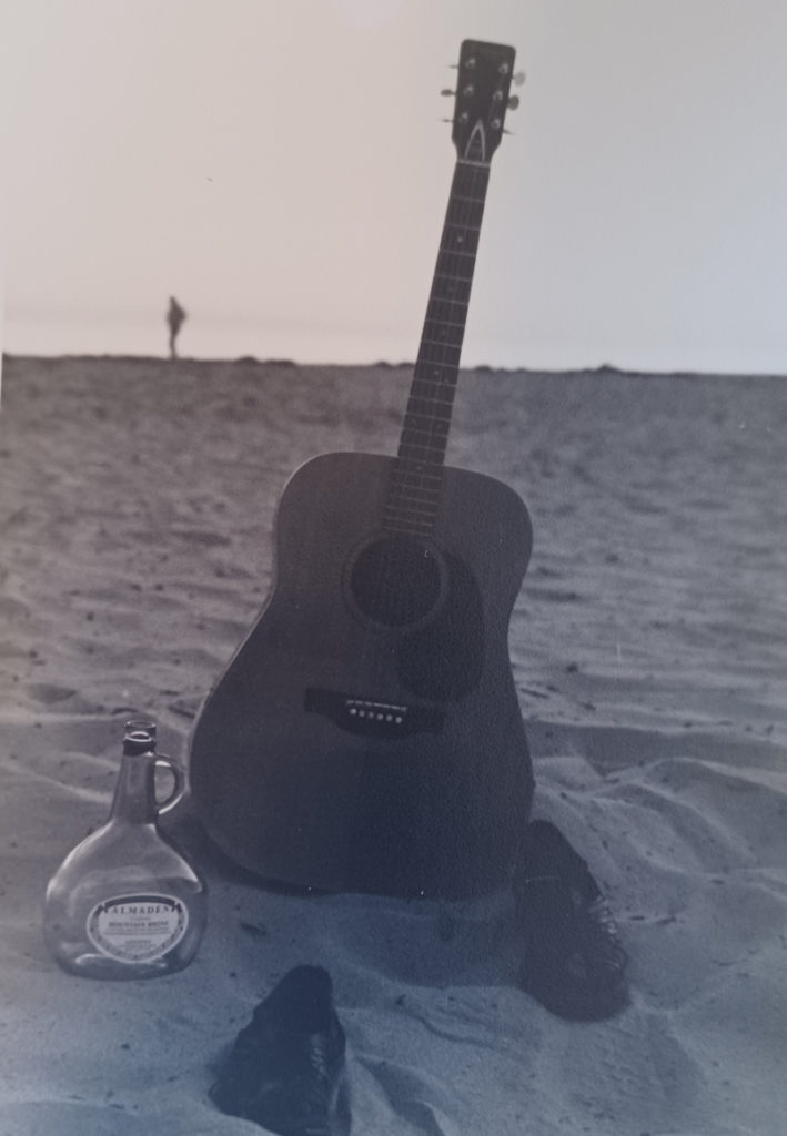 guitar with shoes and empty bottle of wine on beach